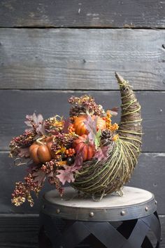 an arrangement of fall flowers and pumpkins in a basket on top of a stool