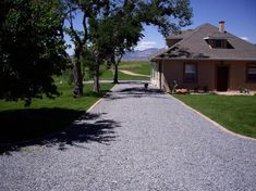 a gravel driveway leading to a house with trees on both sides and grass in the background