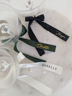 three wine glasses are sitting next to each other on a marble platter with ribbon and name tags