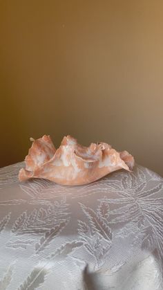 a white table cloth with a pink shell on it's side and a brown wall in the background