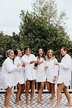 the bridesmaids are all dressed in white robes and holding champagnes while standing together