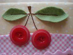 two red buttons sitting on top of a pink and white checkered table cloth next to a green leaf