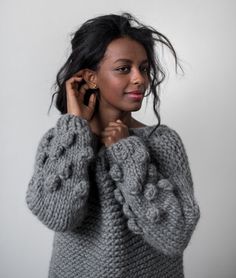 a woman is wearing a gray sweater and holding her hands up to her ear