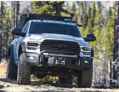 the front end of a silver truck driving on a dirt road in the middle of some trees