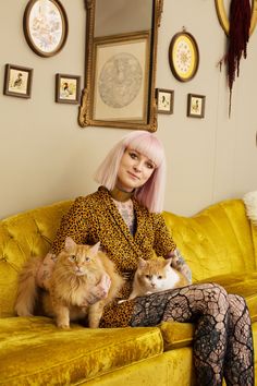 a woman sitting on top of a yellow couch with two cats