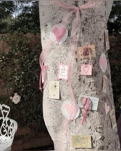 a tree decorated with pink hearts and pictures on it's bark in front of a fence