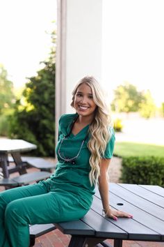 a woman sitting on top of a picnic table smiling at the camera while wearing scrubs