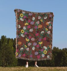 a person standing in front of a blanket with flowers on it and trees behind them