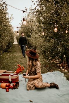 a woman sitting on top of a blanket next to an apple orchard