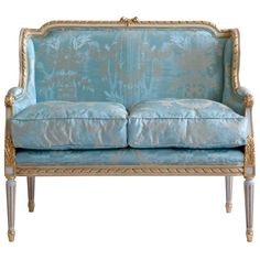 a blue couch with gold trimmings on the arms and back, sitting against a white background