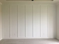 an empty room with white paneling and a ceiling fan in the corner on the far wall