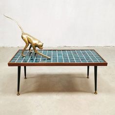 a gold monkey sculpture sitting on top of a blue tiled coffee table with black legs