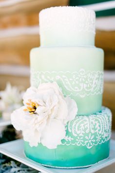 a three tiered cake with white flowers on the top and green frosting below