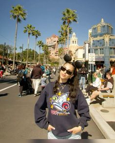 a woman wearing mickey mouse ears standing in the middle of a street with palm trees