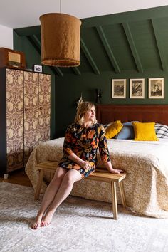 a woman sitting on a bench in front of a bed with green walls and wooden beams