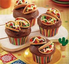 chocolate cupcakes decorated with colorful toppings on a yellow plate next to cactus