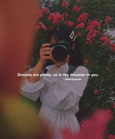 a woman taking a photo with her camera in front of flowers and the words dreams are pretty, so is the dream in you