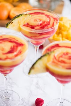 three wine glasses filled with fruit and garnish next to pineapples on a table