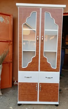 a wooden cabinet with two glass doors on the top and bottom, in front of an orange building