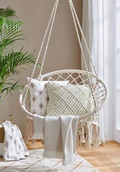 a white hammock hanging from a ceiling in a living room next to a potted plant