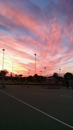 the sun is setting over a tennis court