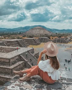 a woman wearing a hat sitting on top of a stone wall next to a pyramid