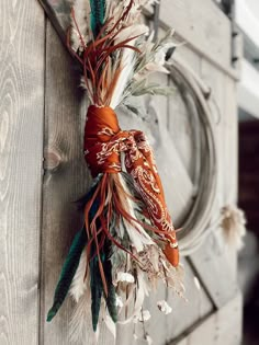 a wreath with feathers hanging on the side of a wooden door, decorated with an orange ribbon