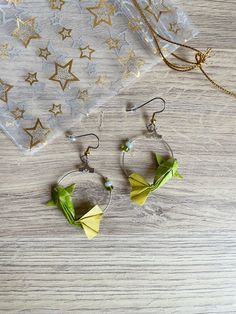 two green origami flowers are hanging from hoop earrings