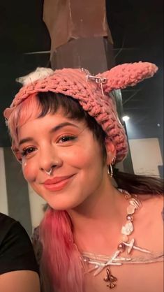 a woman with pink hair and bunny ears on her head smiling at the camera while standing next to a mannequin