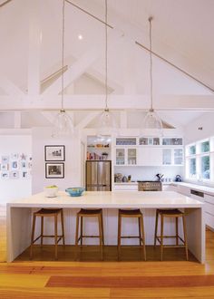 an open kitchen with white cabinets and wooden flooring is pictured in this image, there are three stools at the center of the island