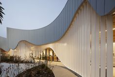 a curved building with white walls and plants in the foreground, along with a walkway leading up to it