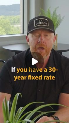 a man wearing a hat is sitting in front of a plant and talking to someone