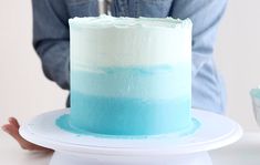 a blue and white cake sitting on top of a plate next to a person's hand