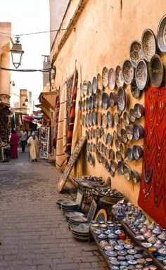 an outdoor market with lots of bowls and plates on the wall next to people walking by