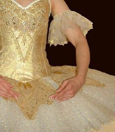 a woman in a gold and white dress sitting on top of a table with her hands behind her back