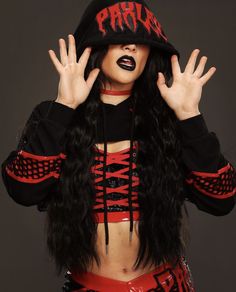 a woman with long black hair wearing a red and black outfit holding her hands up to her face