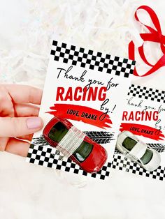 a hand holding a card with two cars on it and a red ribbon tied to the back