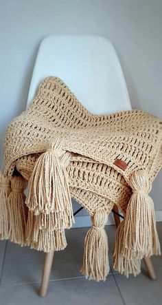 a crocheted blanket sitting on top of a white chair with tassels