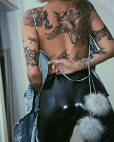 the back of a woman's body with tattoos on her arms and legs, holding a black purse