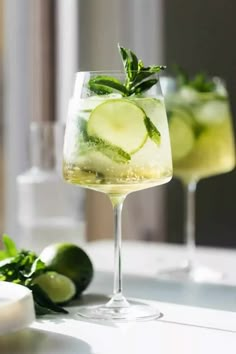 two glasses filled with cucumber, mint and lemonade on top of a table