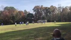 a group of people playing soccer on a field with trees in the backgroud