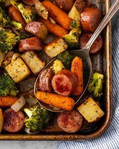 a pan filled with potatoes, broccoli and carrots next to a spoon