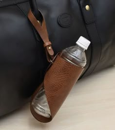 a black duffel bag sitting next to a brown leather purse with a water bottle in it