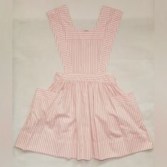 a pink and white striped dress with pockets on the front, sitting on a white surface