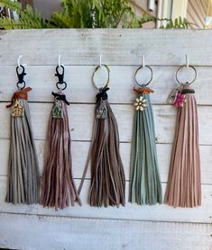 four tasseled key chains hanging on a white wooden board with plants in the background