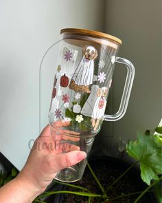 a person holding up a clear glass cup with pictures on the side and flowers in it