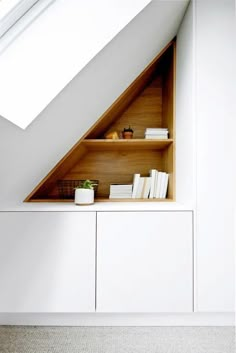 a shelf with books and other items under a slanted roof window in a white room