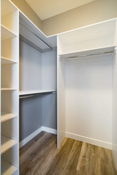 an empty walk in closet with white shelving and wood flooring on the side