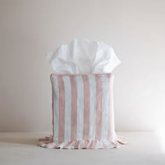 a pink and white striped tissue paper holder with ruffles on the bottom, sitting on a table