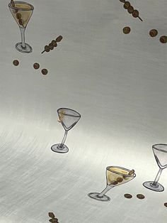 three martini glasses with olives and coffee beans falling from them on a silver surface